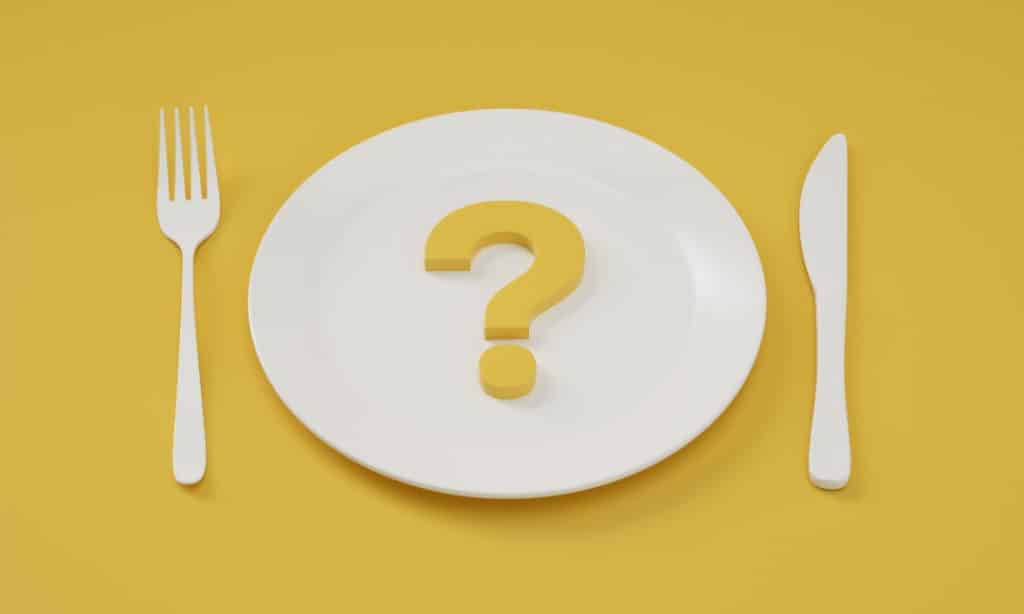 A place setting on a yellow background, the plate has a question mark on it.