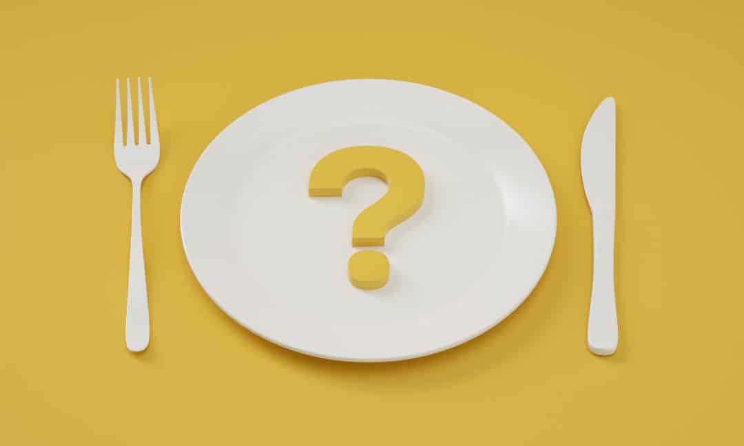 A place setting on a yellow background, the plate has a question mark on it.