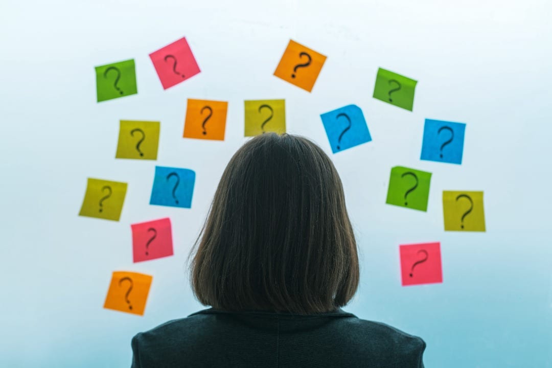 Woman with her back to us looking at colorful post-its with question marks on them.